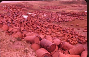 Photo of piles of oil drums on hillside.